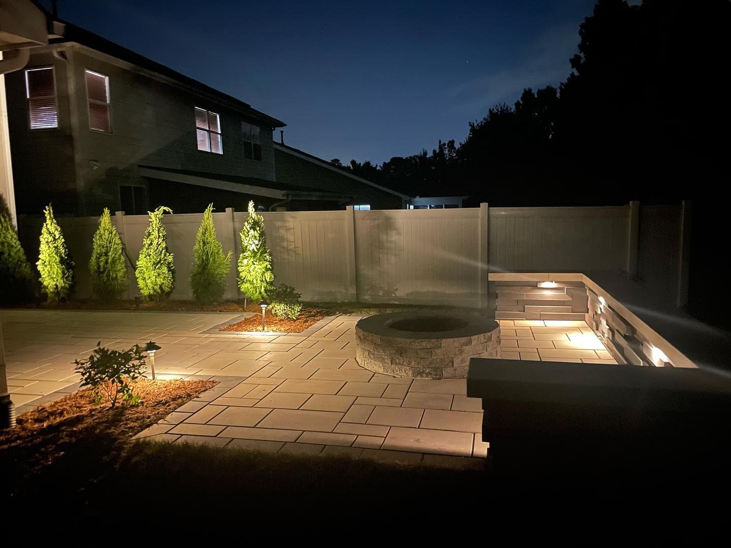 A fire pit is lit up at night in a backyard.