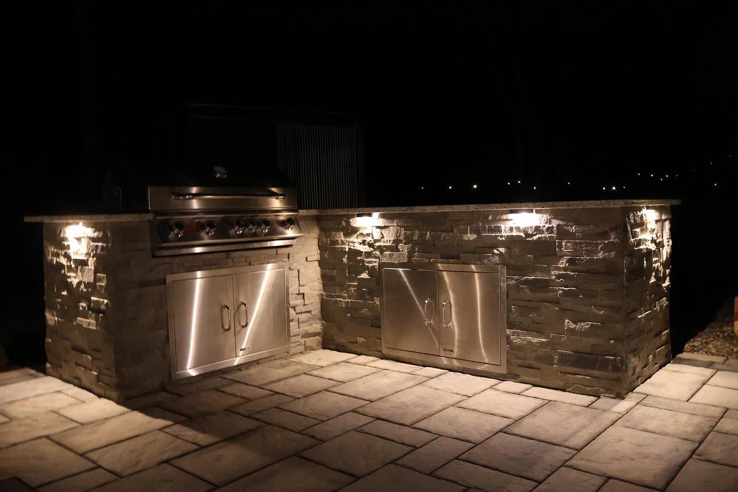 A stainless steel grill is sitting on a stone patio at night.