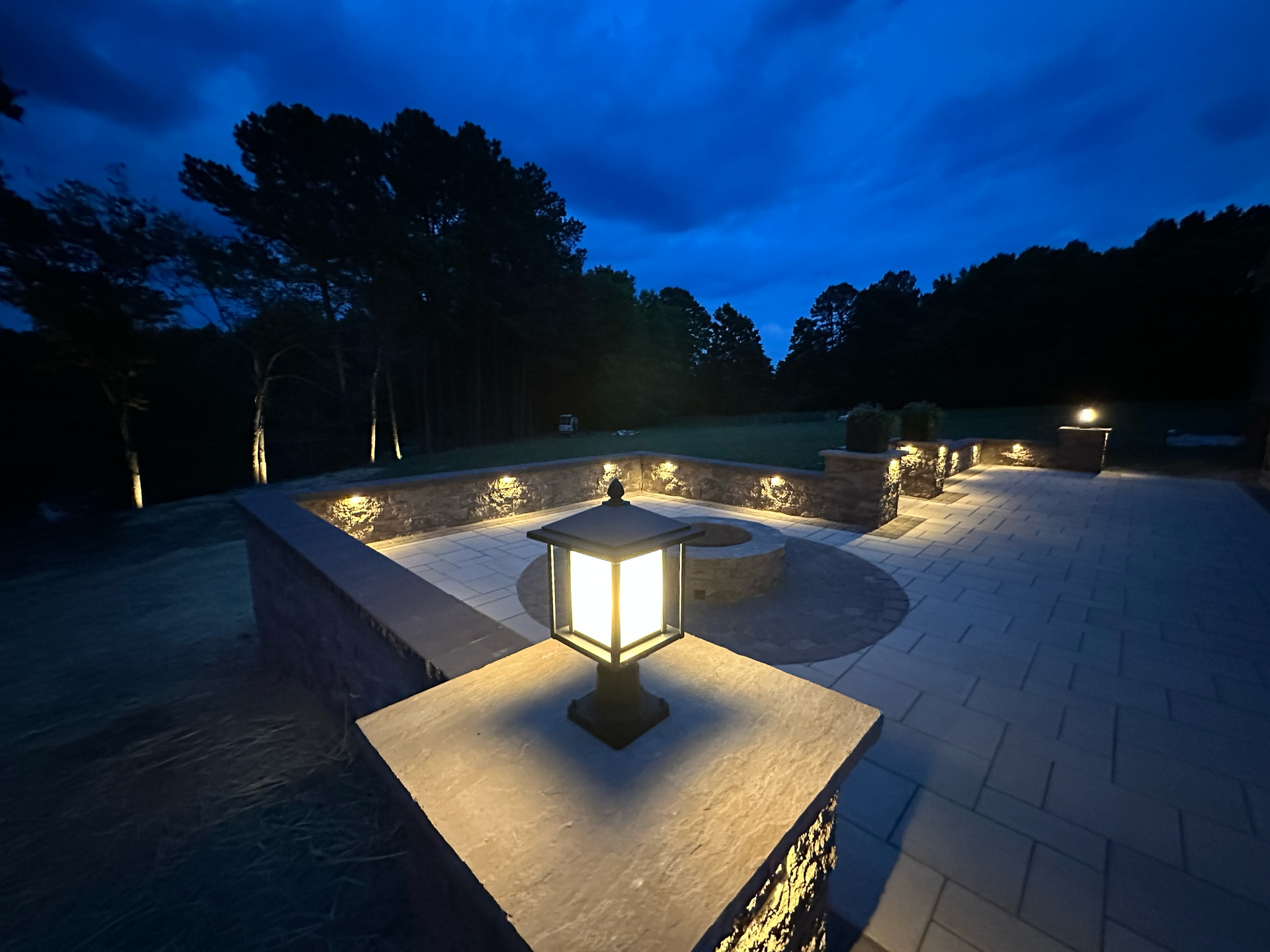 A patio with a fire pit and chairs is lit up at night.
