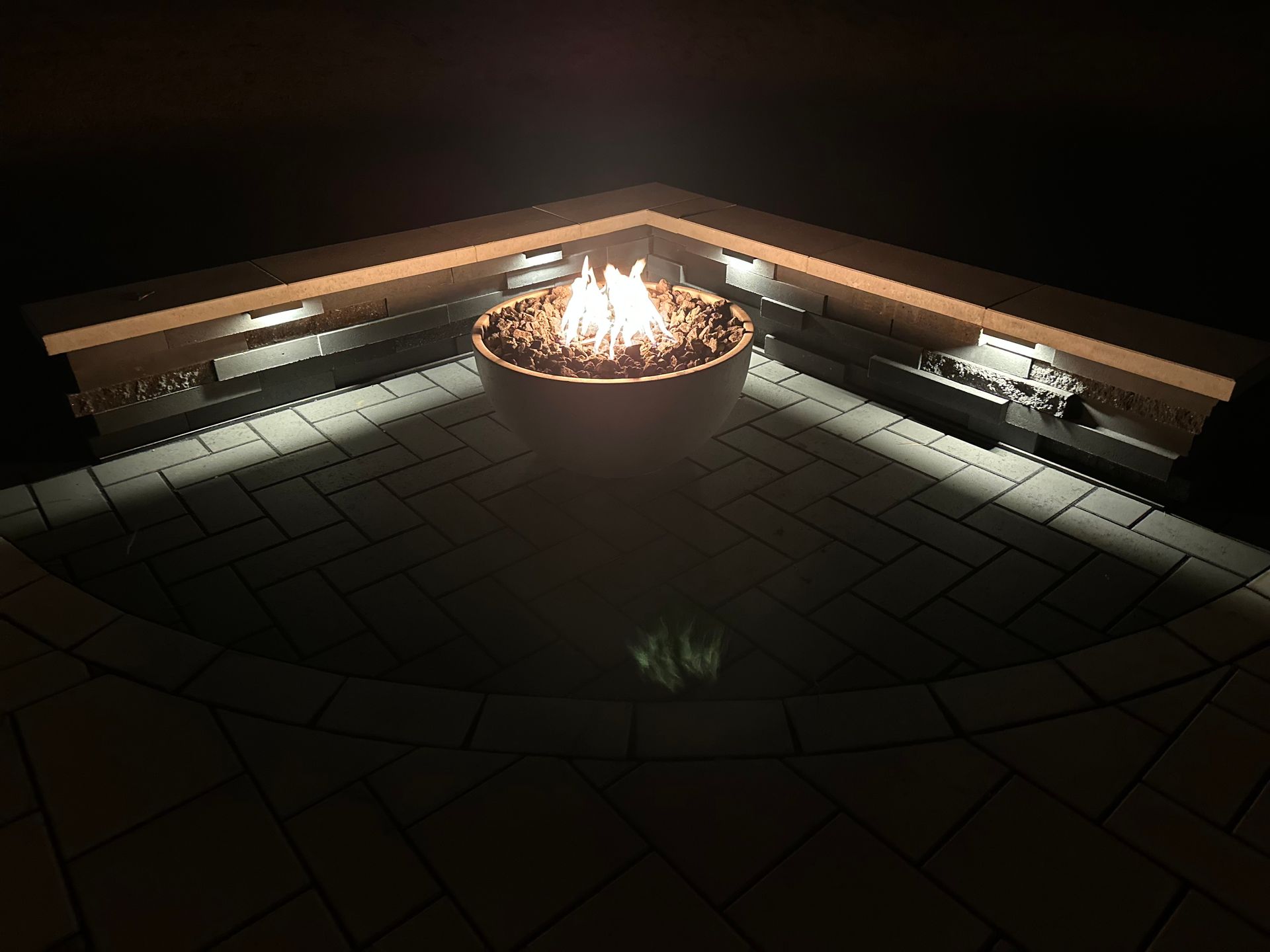 Fire pit lit in a corner setting, illuminating a tiled patio at night.