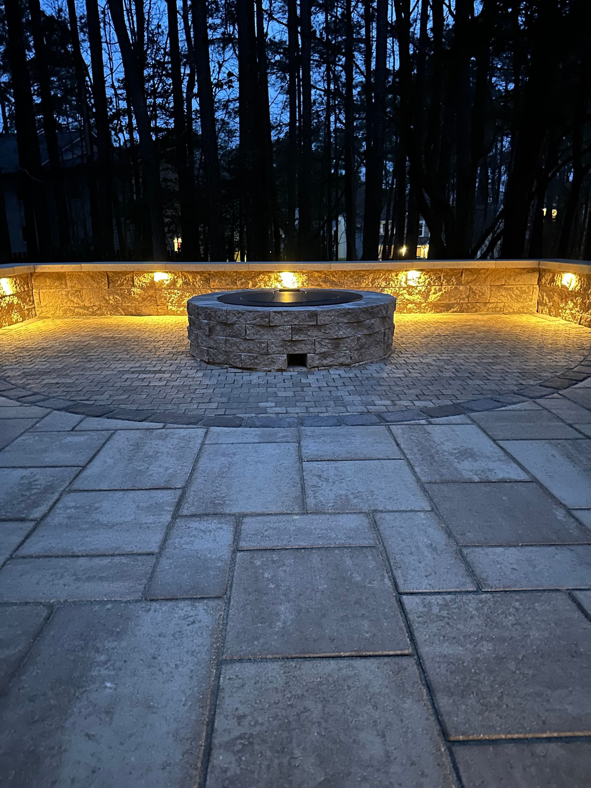 A patio with a fence and trees is lit up at night.
