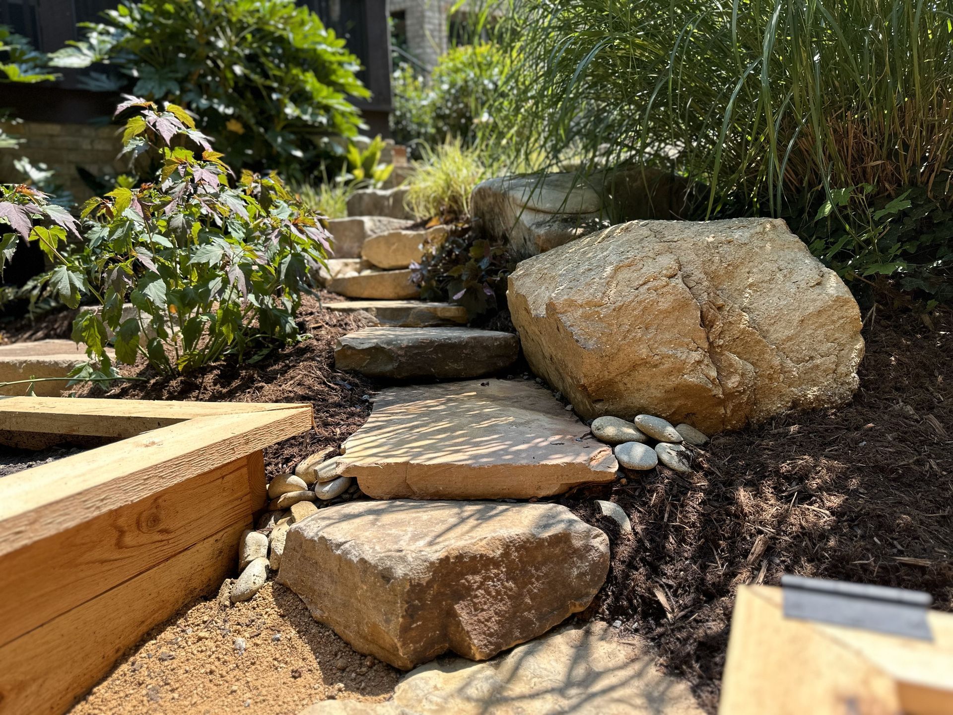 A stone walkway in a garden with a large rock in the middle.