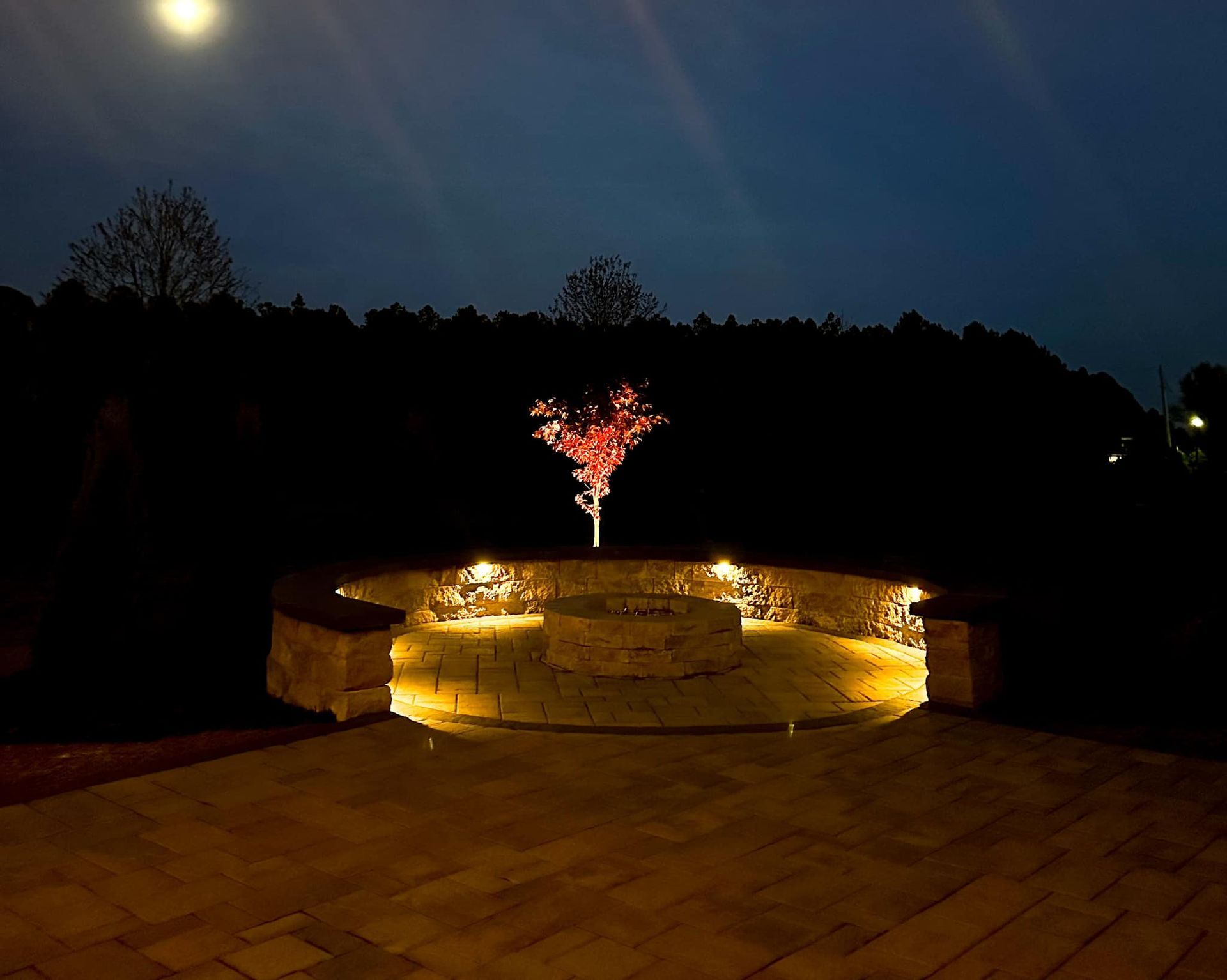 A fire pit is lit up at night with a tree in the middle