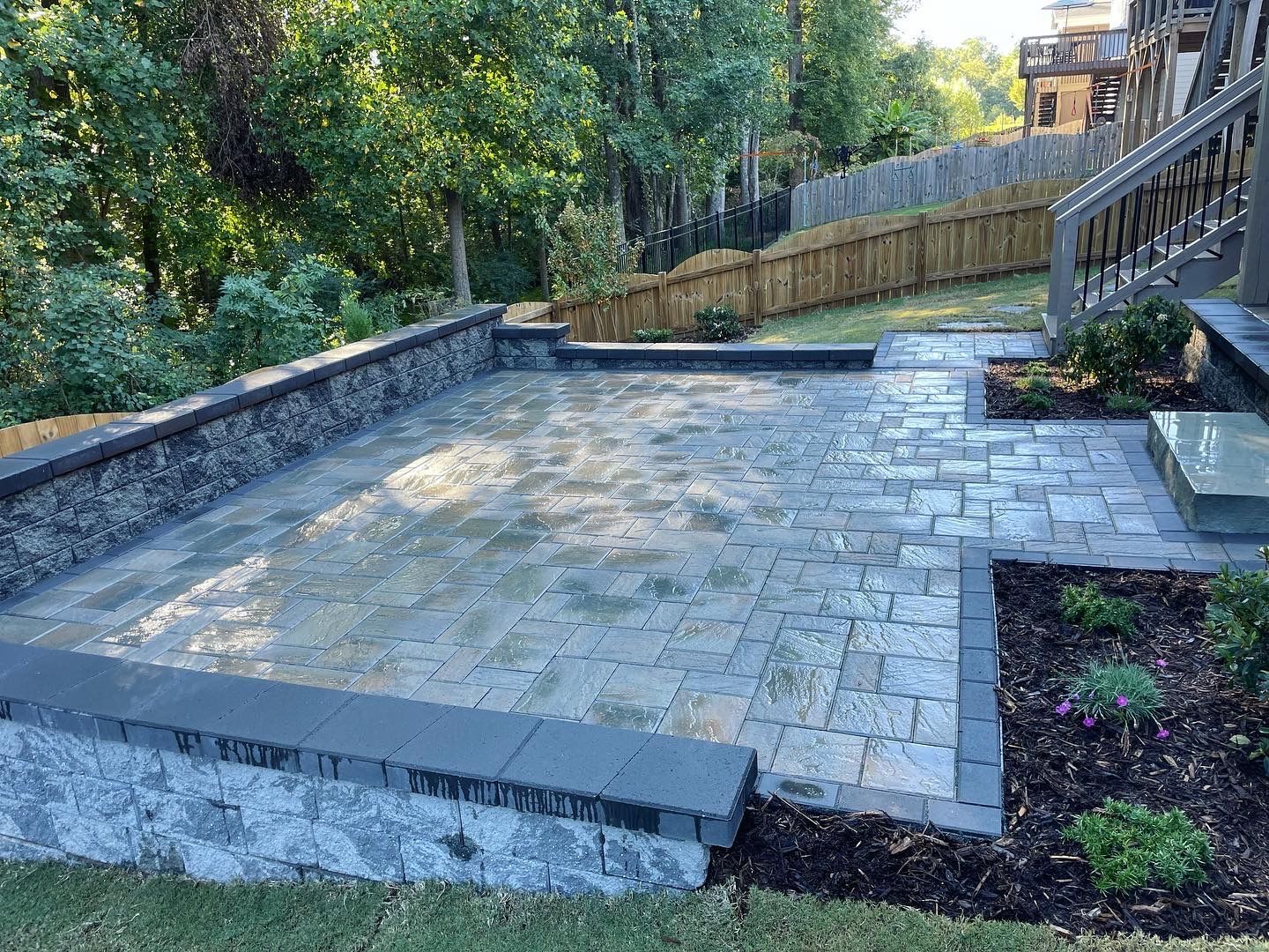 A patio with a stone wall and stairs in the backyard of a house.