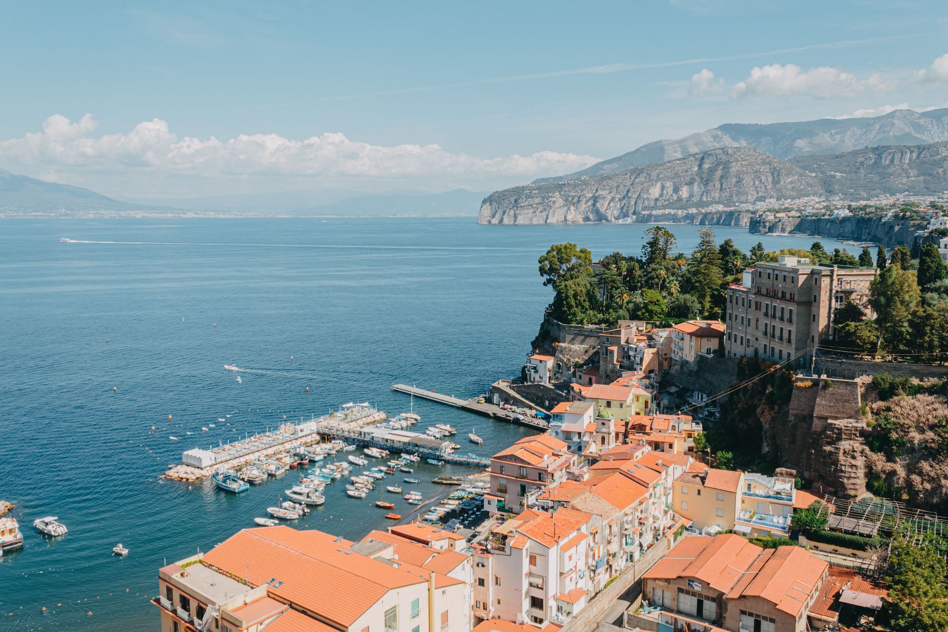 Coastal harbor town with orange rooftops, marina, and cliffs beside a calm blue sea