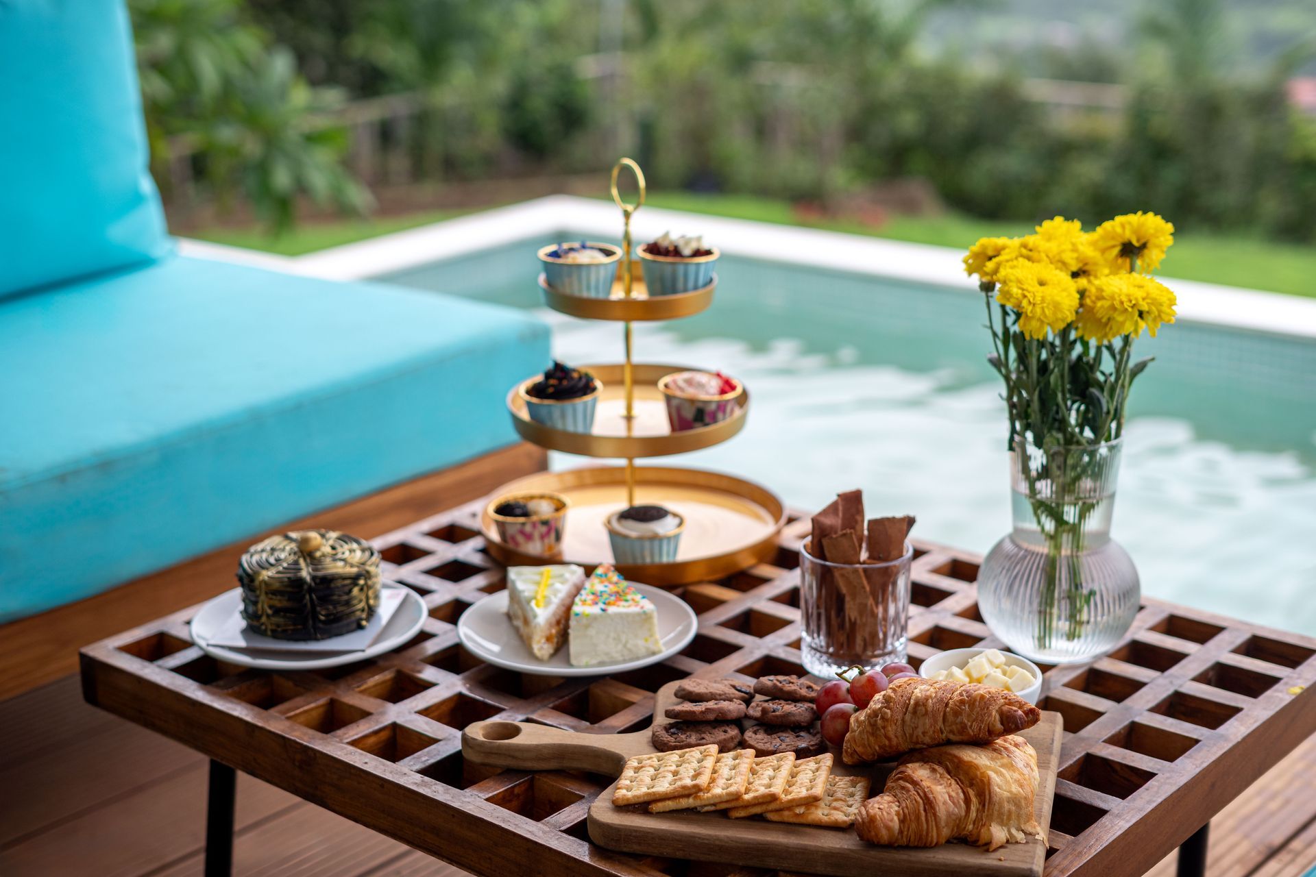 Outdoor tea and pastries on a wooden table with yellow flowers and a turquoise sofa nearby
