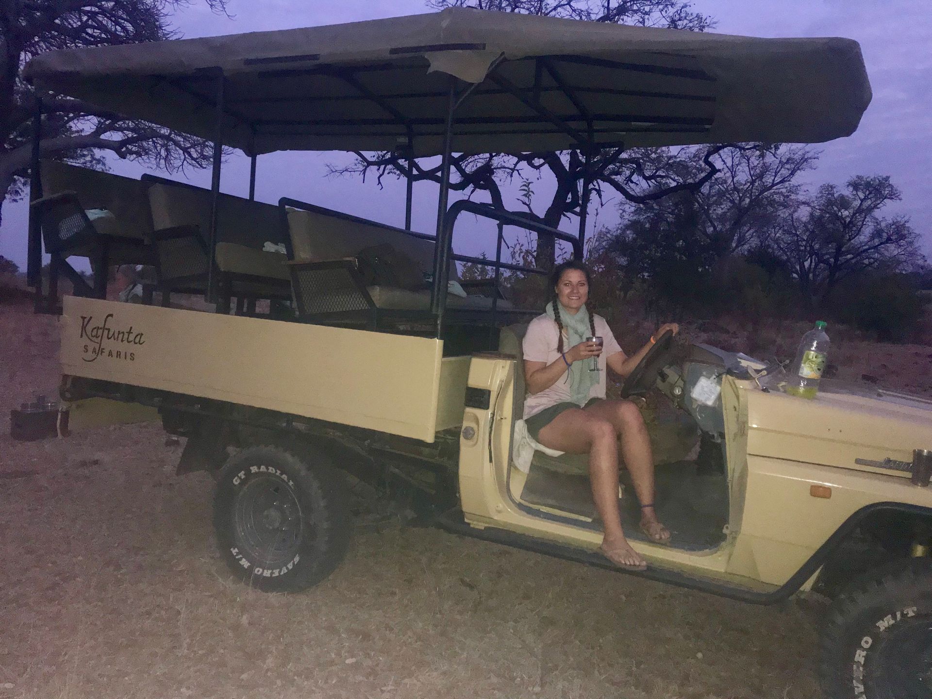 Open safari jeep with canopy parked outdoors; a person sits in the front seat at dusk.