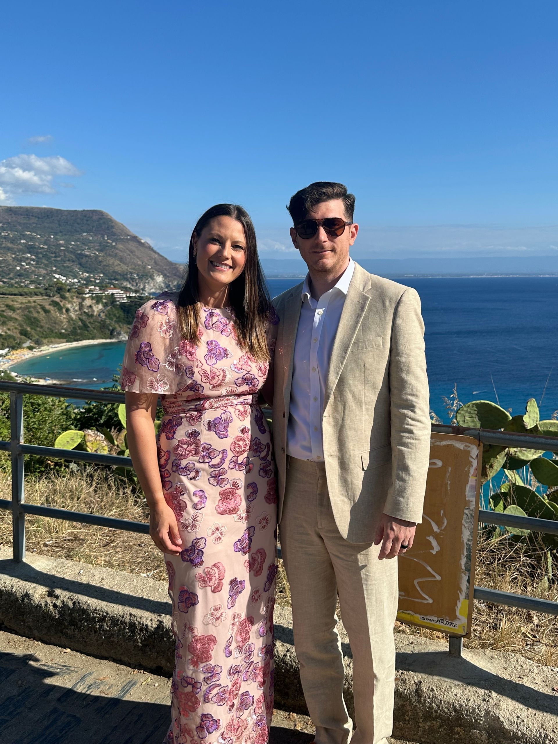 Two people posing by a coastal overlook with ocean and beach in the background
