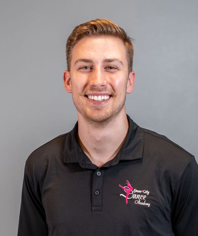 A young man wearing a black polo shirt is smiling for the camera.