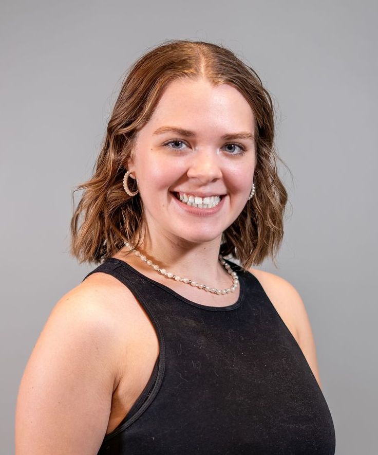 A woman wearing a black tank top and a necklace is smiling.