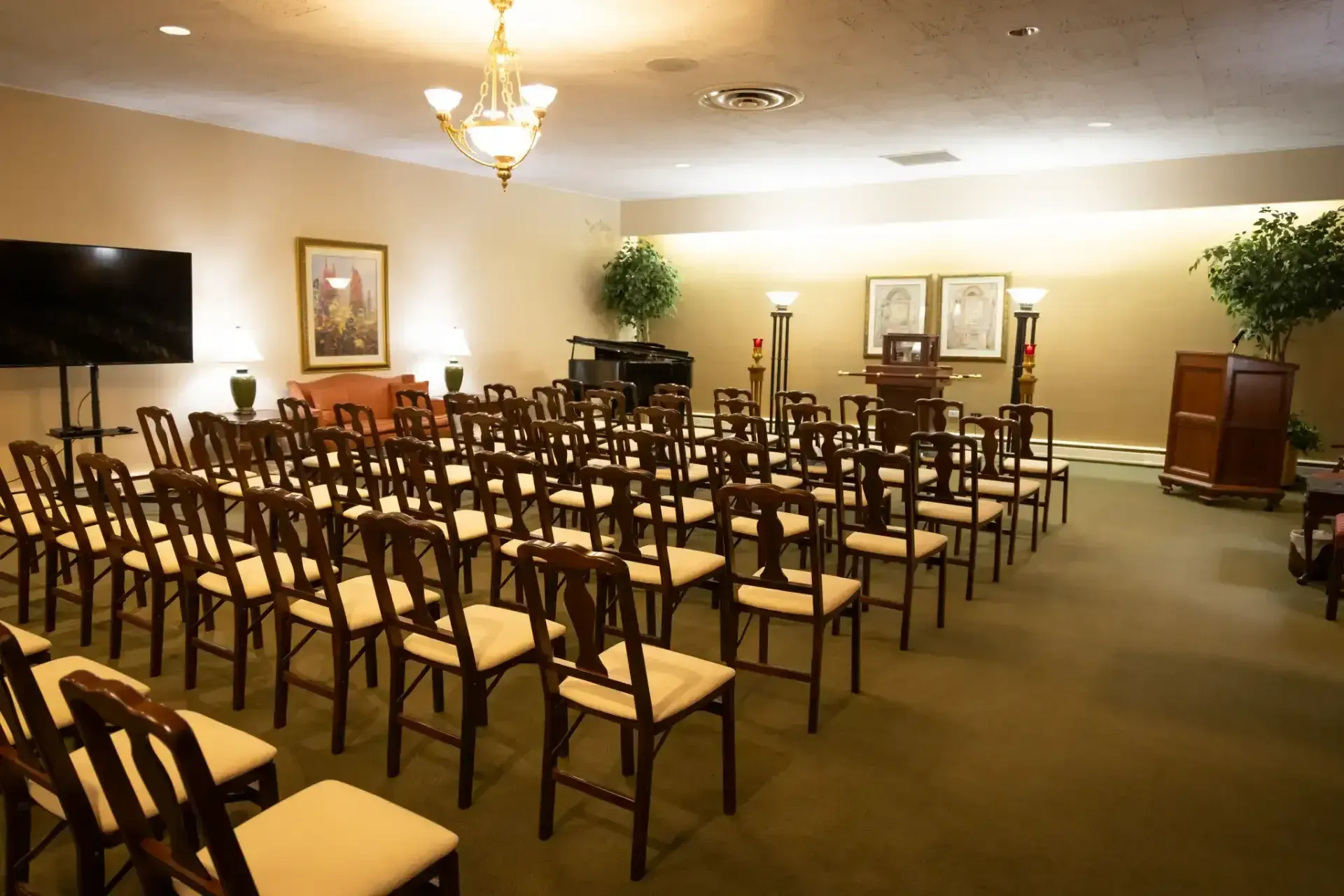 Empty conference room with rows of chairs, a wall-mounted TV, and a podium under warm lighting