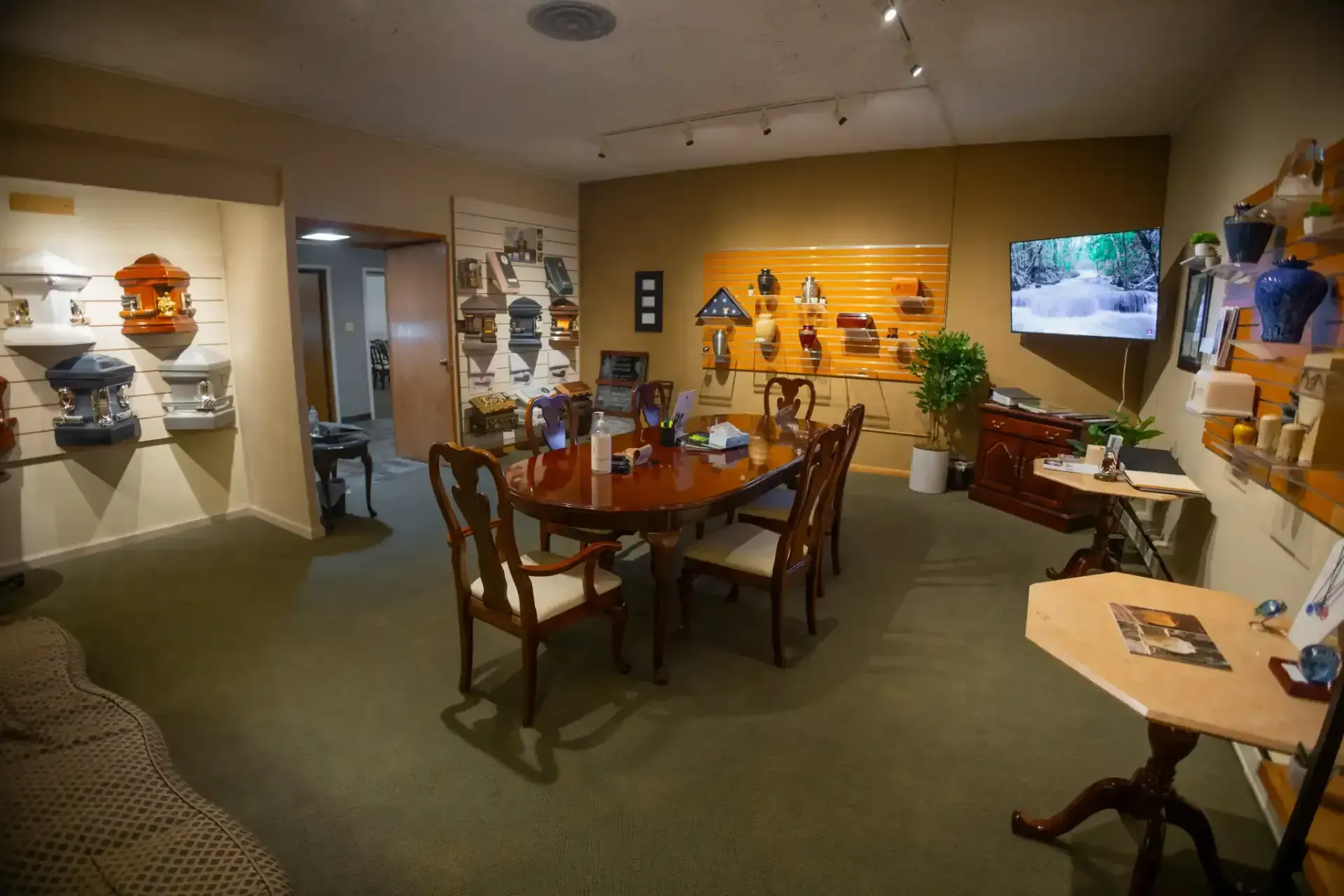 Museum exhibit room with a central wooden table display, wall panels, and a TV screen on the right.
