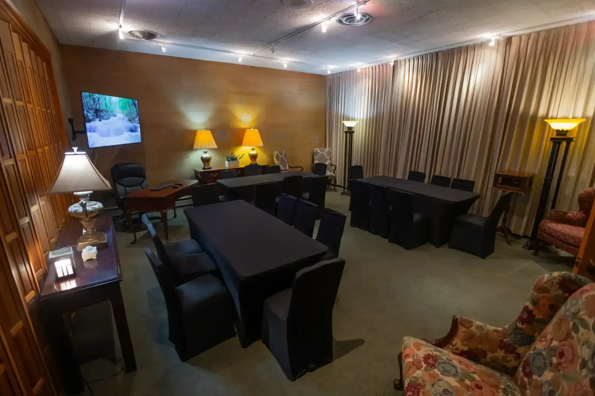 Cozy living room with dark furniture, warm lamps, striped curtains, and a wall-mounted TV.