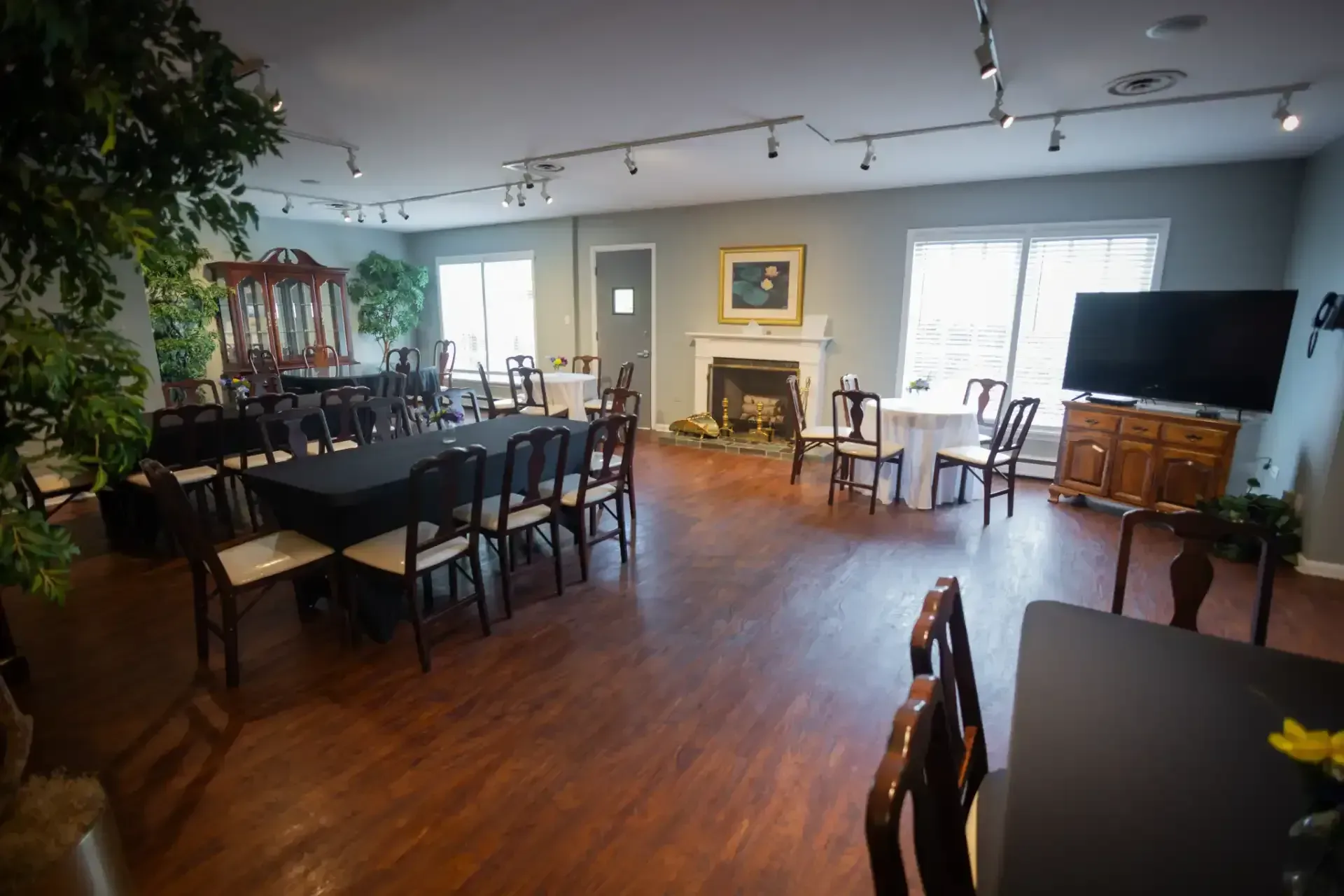 Empty dining room with dark tables and chairs, wood floors, fireplace, TV, and large windows