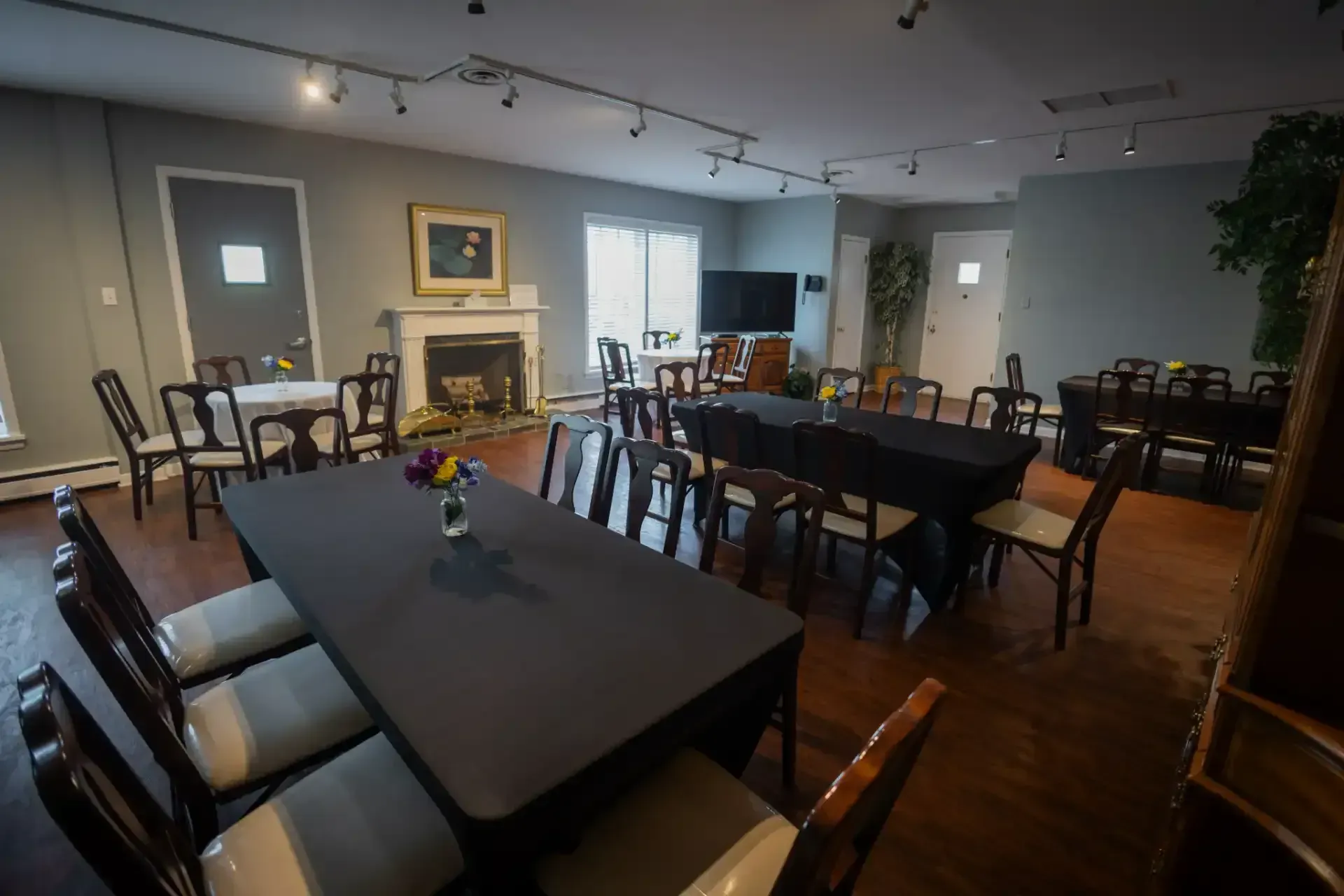 Empty dining room with dark wood tables, chairs, and a fireplace under string lights