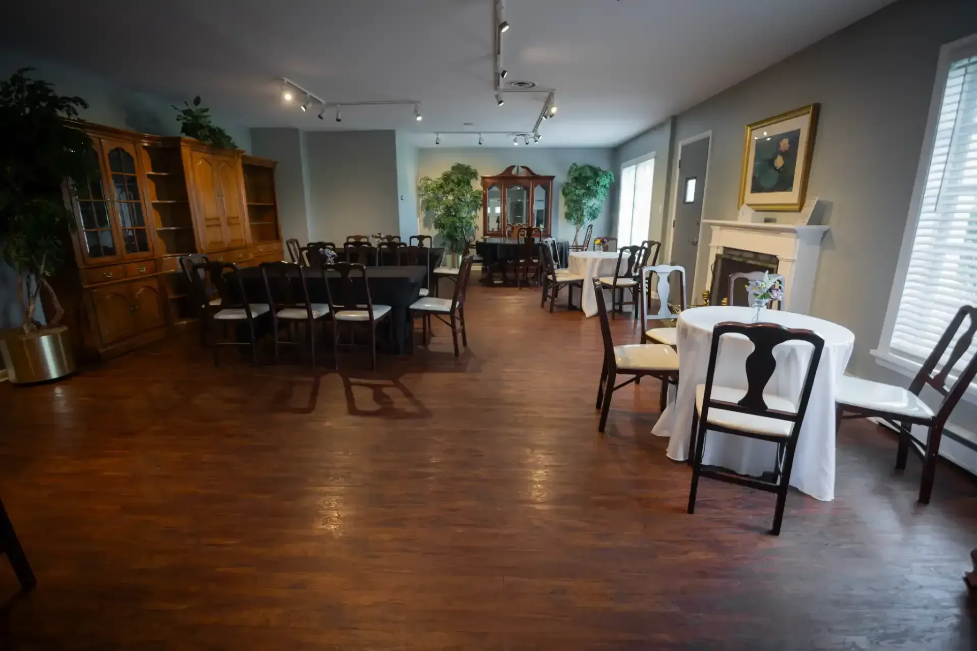 Spacious dining room with wooden floors, multiple tables and chairs, cabinets, plants, and wall art.
