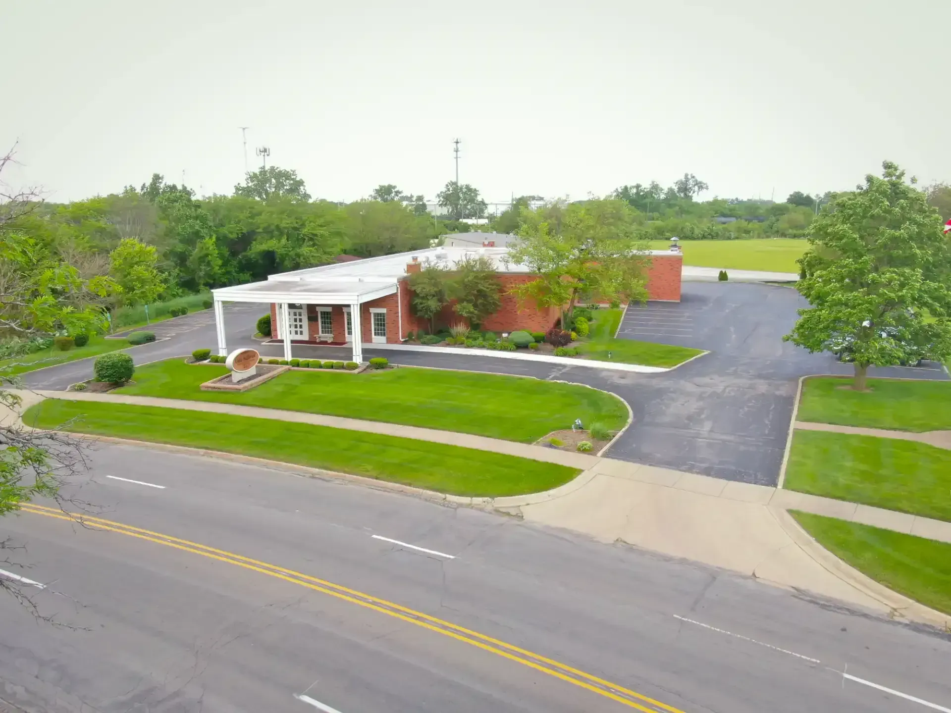 Aerial view of a small brick-and-white office building with a parking lot and road in front.