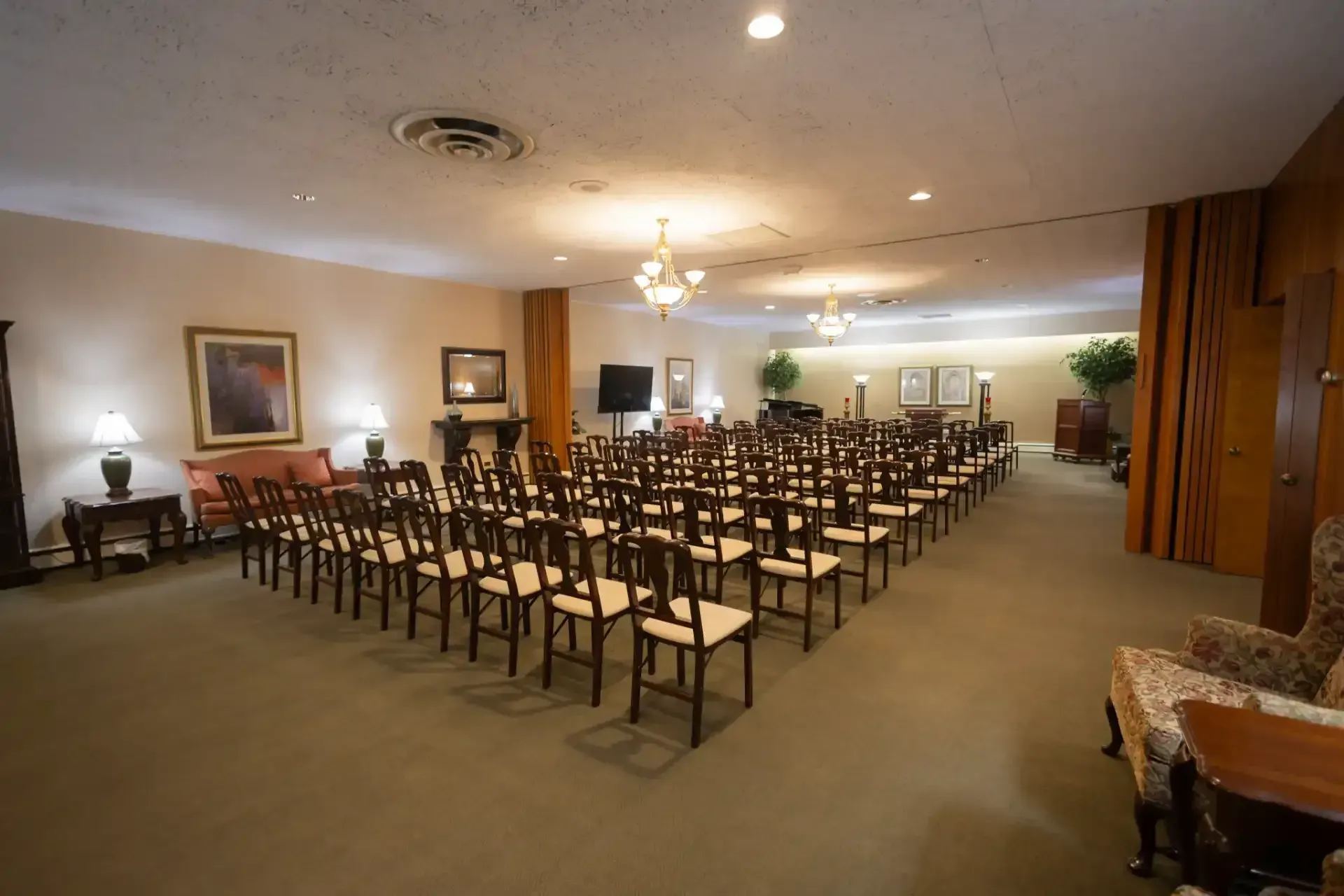 Large empty banquet hall with rows of chairs facing a front area, warm lighting, and beige carpet