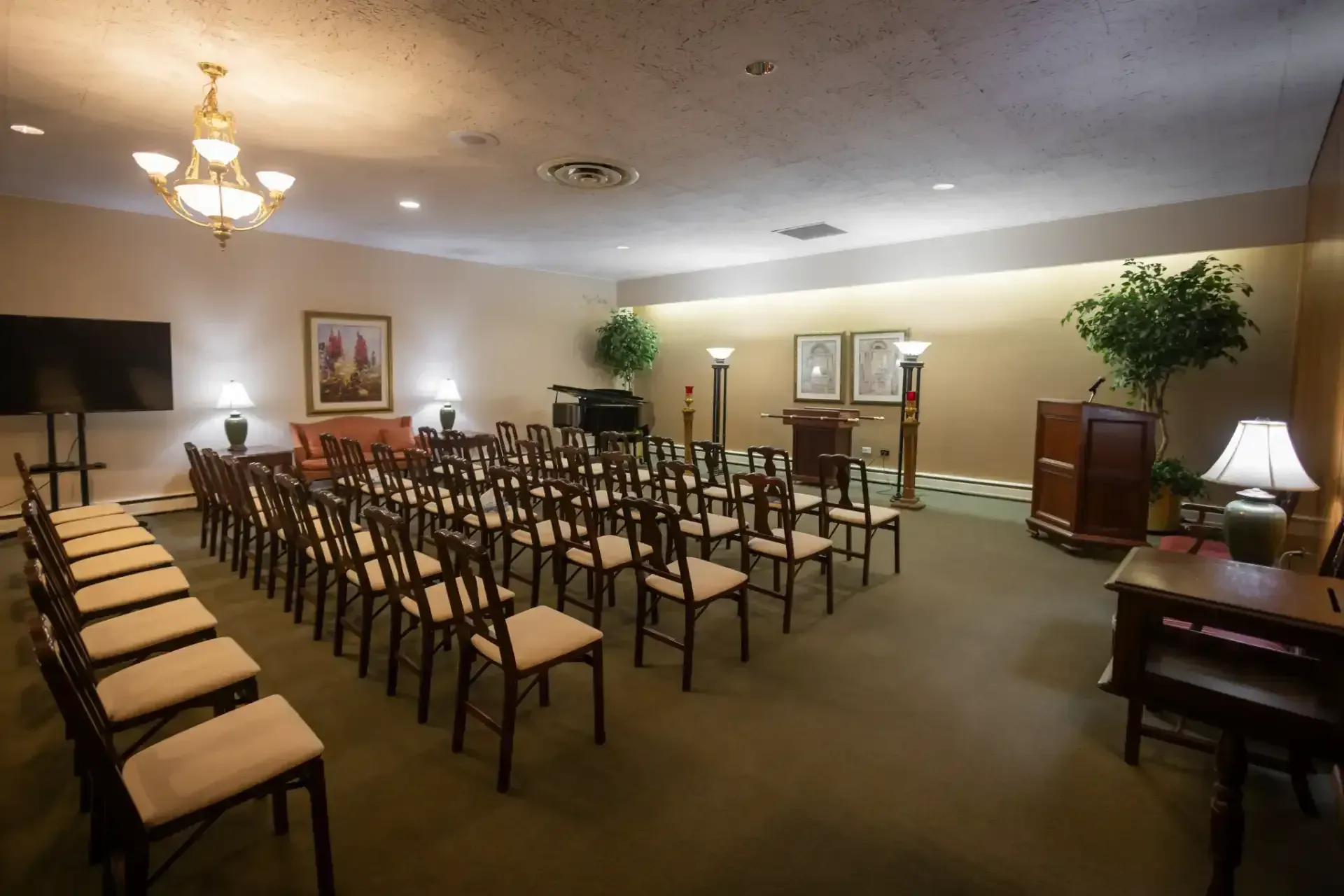Small meeting room with rows of chairs facing a front display, lamps, and framed wall art