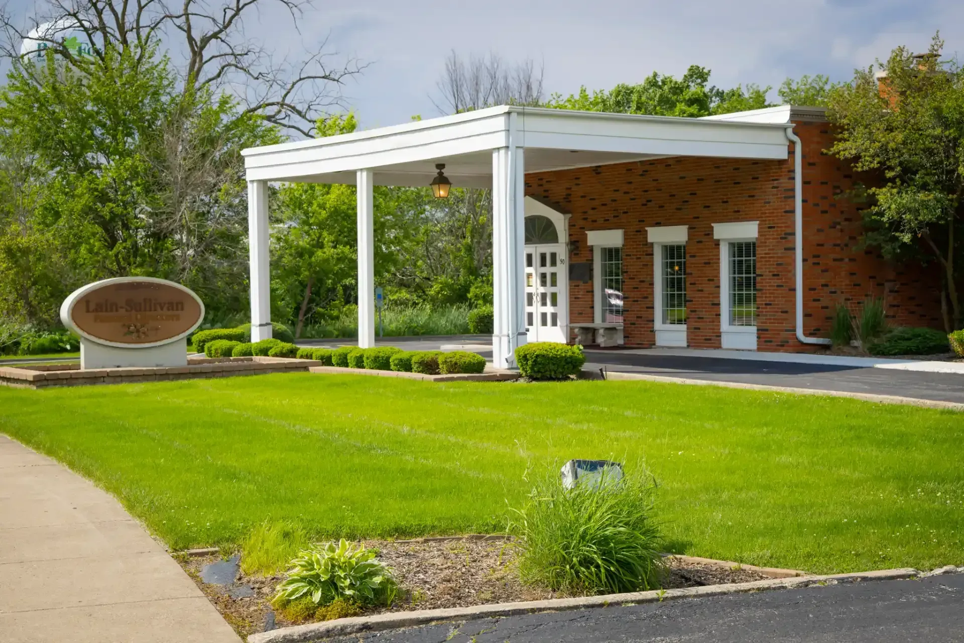Brick building entrance with white canopy, green lawn, and landscaped walkway