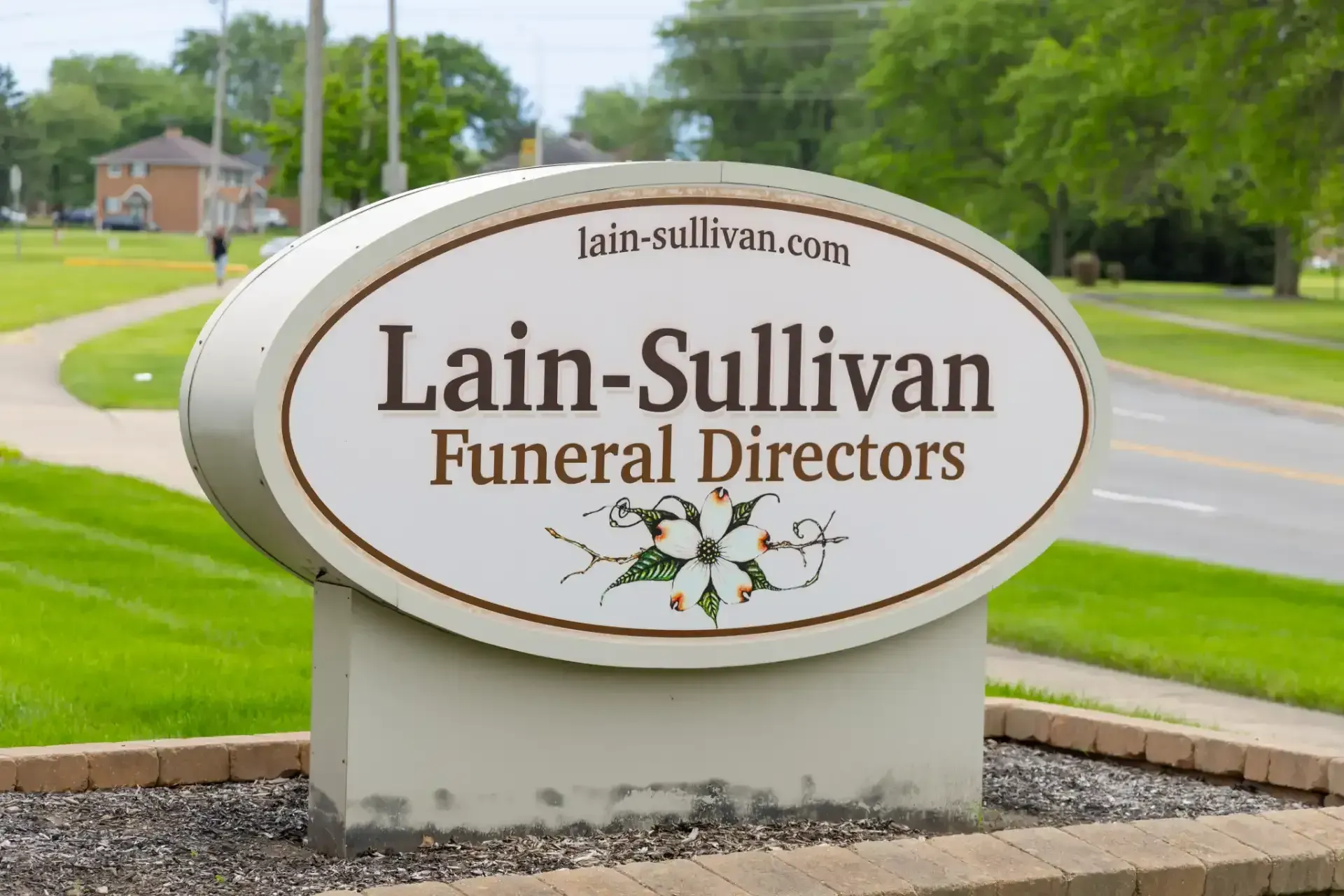 Lain-Sullivan Funeral Directors roadside sign with white oval lettering and floral design