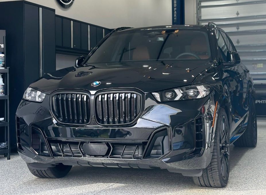 Black BMW SUV parked indoors in a garage, front view with headlights off.