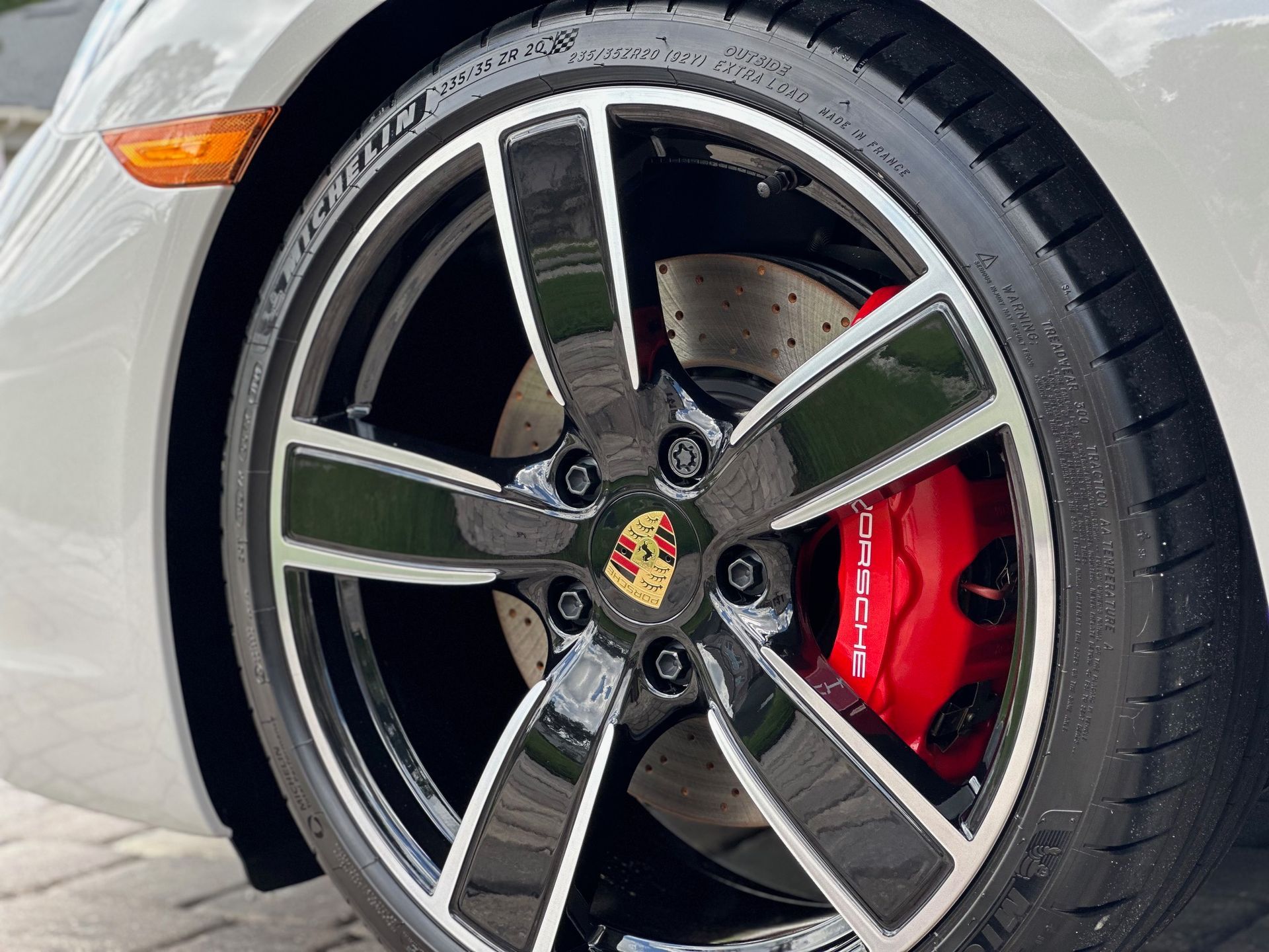 Close-up of a white Porsche car wheel with black and silver spokes, a red brake caliper, and a Michelin tire.