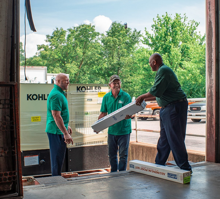 Three workers in green shirts unloading construction materials at a warehouse doorway
