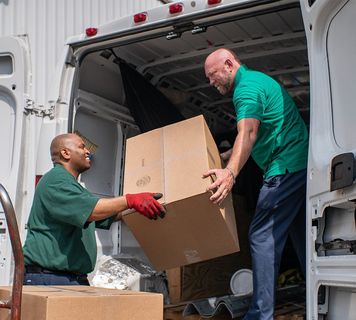 Two movers loading a large cardboard box into a moving truck