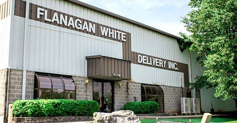 Flanagan White Delivery Inc. building exterior with brick entry, green shrubs, and corrugated metal facade