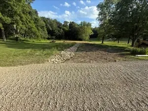 Rocky gravel path through a green park with trees and blue sky.