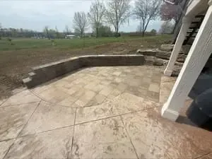 Patio with stone pavers and curved retaining wall overlooking a grassy yard and bare trees