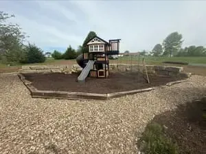 Playground with a small slide and climbing structure in a gravel park area under cloudy skies