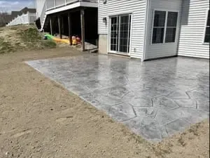 Stamped concrete patio beside a white house, next to a dirt yard and under-construction area.