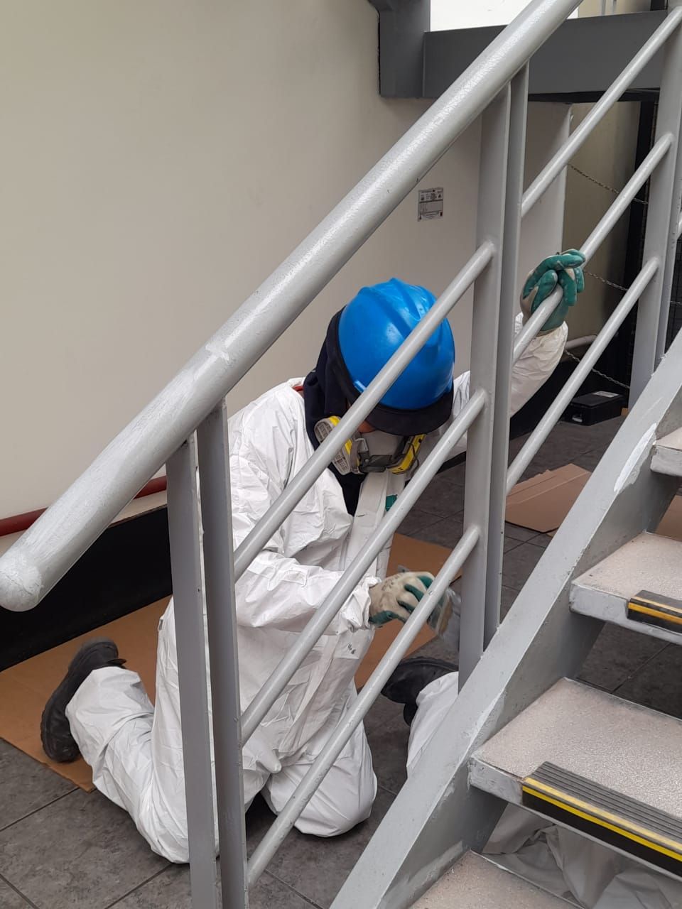 Persona con traje de protección pintando barandilla de escalera.