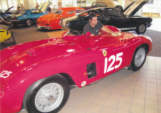 A man sits in a red sports car with the number 125 on the side