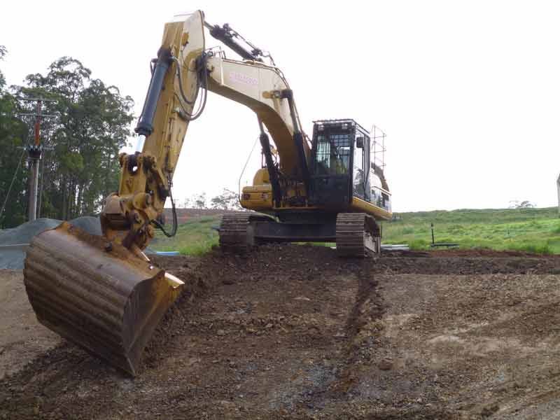 Yellow Excavator Digging Into a Dirt Mound on A Construction Site — Jim Anderson Earthmoving Pty Ltd in Coopernook, NSW