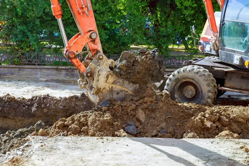 Orange Excavator Bucket Digging Soil in a Street, Sunlight — Jim Anderson Earthmoving Pty Ltd In Old Bar, NSW