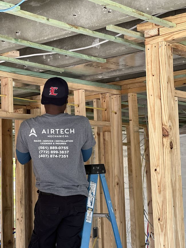 Man working on a ceiling. He's wearing a grey Airtech shirt and a black hat. Construction site.
