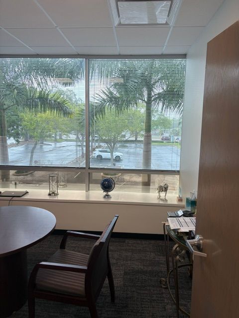 Office with large window, round table, chairs, and a parking lot view outside.