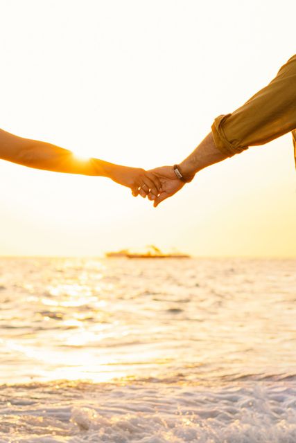 Two people holding hands over waves at sunset on a beach