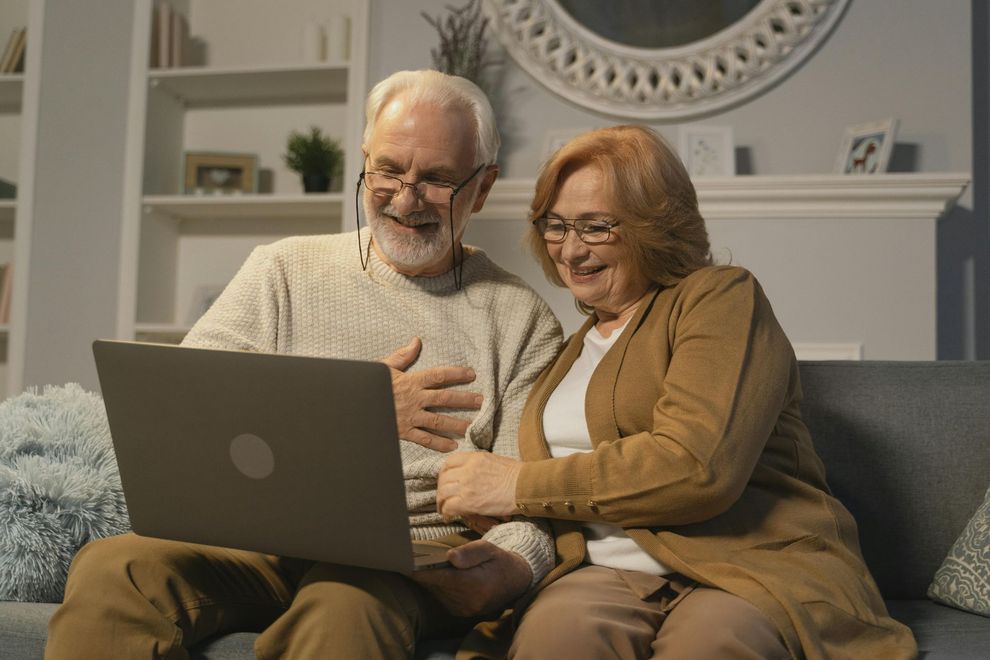 Two people smiling and using a laptop on a couch in a cozy living room