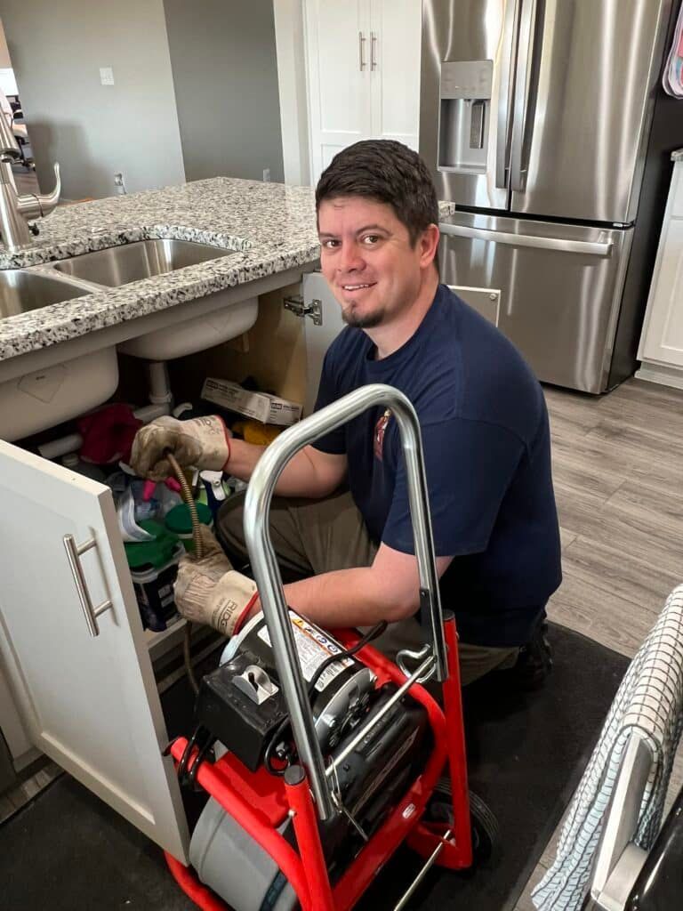 Man smiling while sitting in a red in a kitchen beside an open cabinet and stainless steel fridge