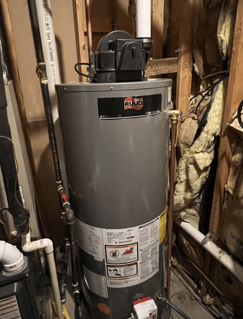 Gray water heater in a utility room with exposed pipes and insulation around it