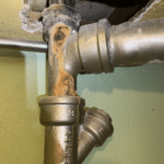 Rusty pipe junction with a green wall and a metal fitting underneath