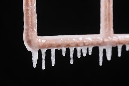 Icy white icicles hanging from a pink metal railing against a black background