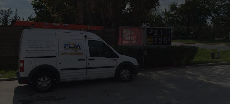 A white van with orange ladder parked near a gas station price sign with green bushes.