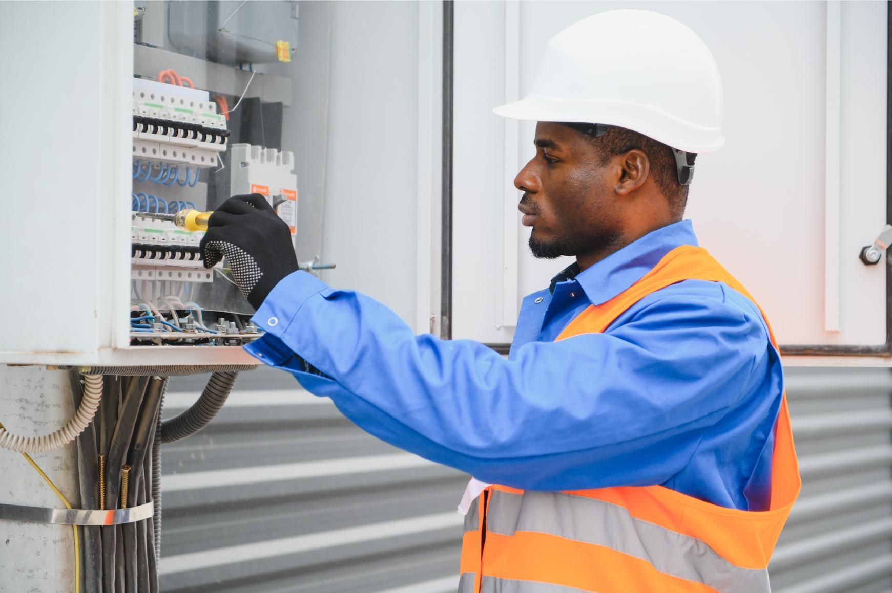 Electrician in hard hat and safety vest working on electrical panel.