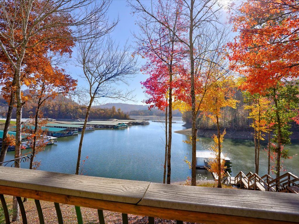 Autumn lake view with colorful trees, docks, and a wooden railing in the foreground.