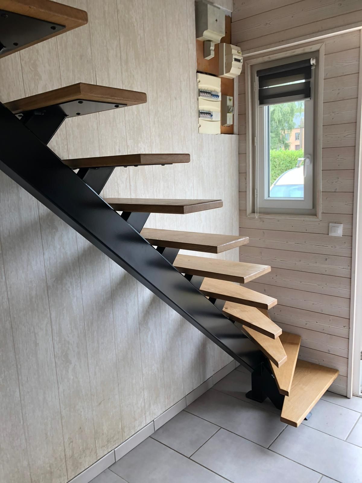 Escalier moderne avec marches en bois, structure en métal noir et fenêtre.